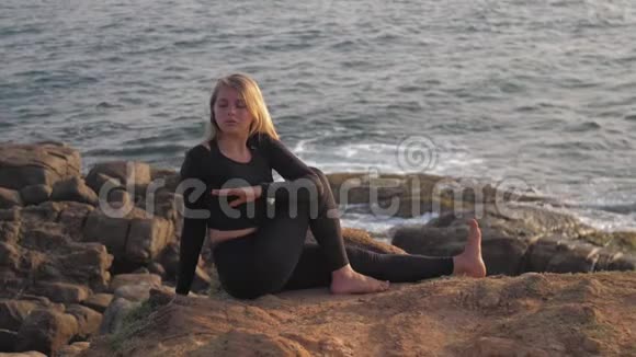 穿黑色运动服的漂亮女孩坐在灰色岩石悬崖上视频的预览图