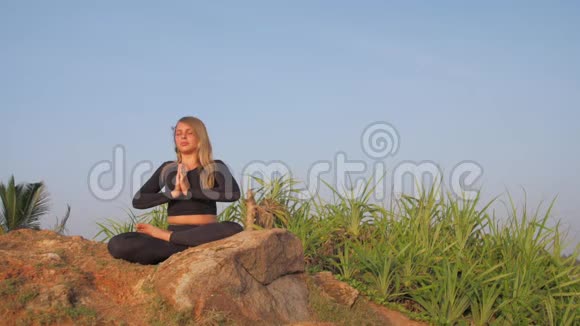 穿着运动服的女士坐在灰色岩石悬崖上做瑜伽姿势视频的预览图