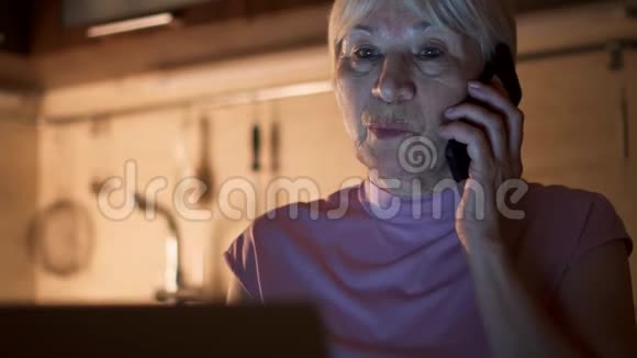 高级妇女晚上从家庭办公室用笔记本电脑工作自由职业者晚上用手机聊天视频的预览图