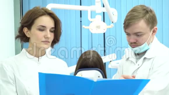 持文件夹的男女牙医在牙科椅上的病人面前讨论治疗问题视频的预览图
