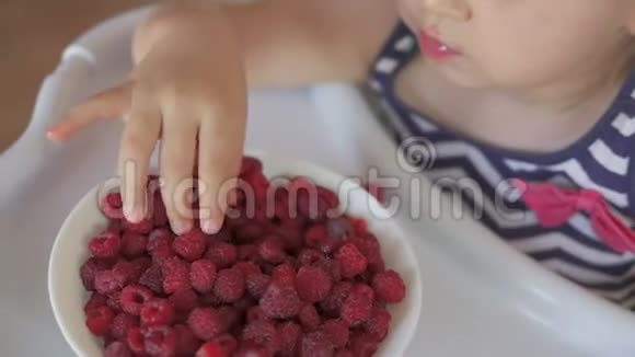 一个小女孩坐在孩子们桌子旁吃成熟的红树莓视频的预览图