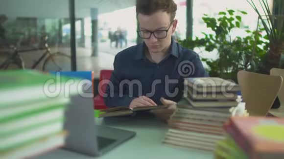 英俊的男子正在图书馆桌上学习许多书视频的预览图