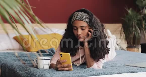 每天早晨躺在床上看智能手机视频的年轻女子视频的预览图