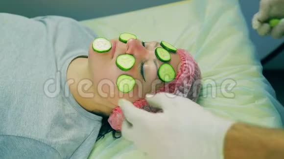 戴手套的男性美容师的手从女人的脸上取出黄瓜视频的预览图