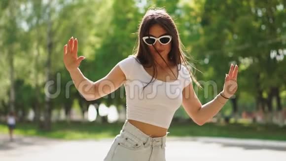 穿着短牛仔短裤和白色T恤的女孩在阳光明媚的一天骑着陀螺滑板车慢动作玩得很开心视频的预览图
