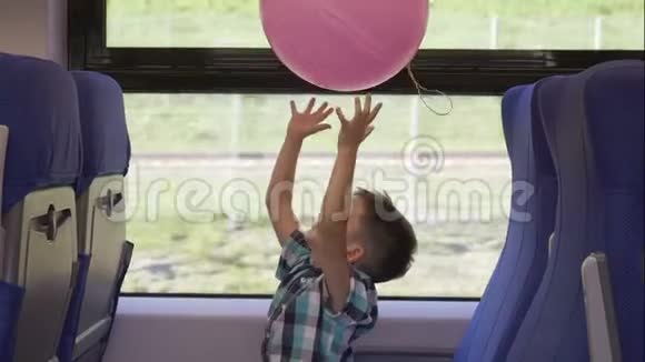 可爱的小男孩在火车上玩粉红色的气球而它在移动儿童度假和旅游视频的预览图