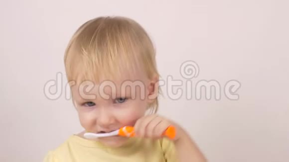 一个金发白种人的小女孩用牙刷刷牙在白色背景的特写镜头上笑视频的预览图