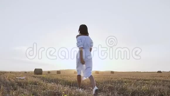 一个年轻可爱的女人在日落时快乐地穿过一片金色的田野带着草捆快乐的女孩享受和奔跑视频的预览图