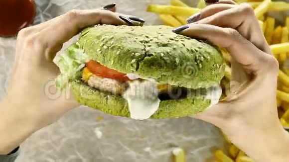 美甲的女人手里拿着一个多汁的大汉堡里面有肉馅饼和一个绿色的面包女人双手旋转视频的预览图