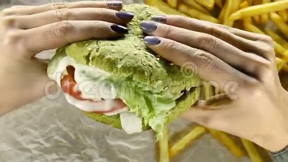 美甲的女人手里拿着一个多汁的大汉堡里面有肉馅饼和一个绿色的面包女性手在旋转视频的预览图