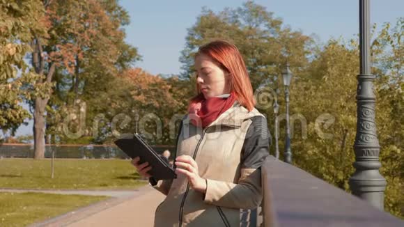 有狐毛的女孩站在户外在阳光明媚的天气里使用平板电脑并在网上订购视频的预览图