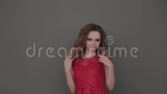 美丽的年轻女孩穿着红色的裙子在灰色的背景上摆姿势视频的预览图