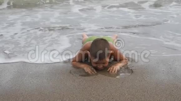 孩子躺在海浪中的沙岸上男孩在海滩上划沙孩子洗了海浪视频的预览图