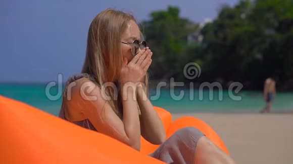 年轻女子一边咳嗽一边坐在热带海滩的充气沙发上旅行疾病概念视频的预览图