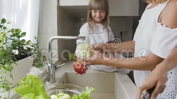 年轻漂亮的妈妈和她可爱的两个女儿一起在厨房的水槽里洗蔬菜准备做饭视频的预览图