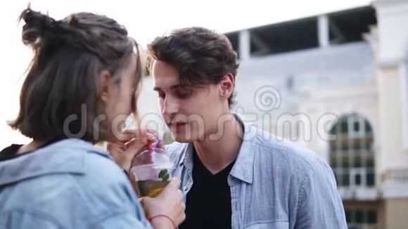 年轻夫妇穿着蓝色衬衫的侧视图是用吸管从塑料杯中一起喝茶女人轻轻亲吻视频的预览图