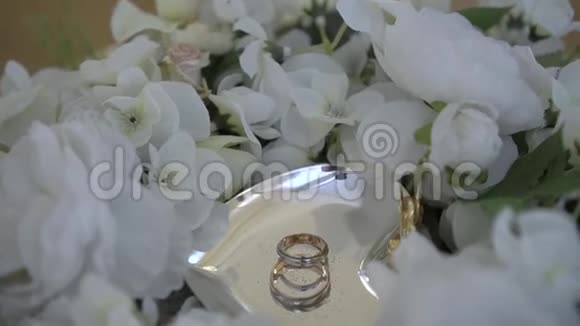 一个金属碟子上的金色结婚戒指上面环绕着一束白色玫瑰视频的预览图