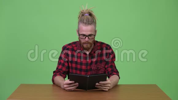 英俊的留胡子的时髦男人靠木桌子看书视频的预览图