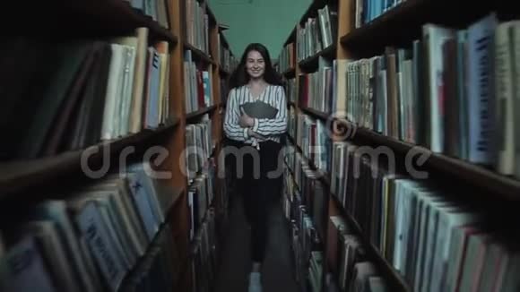 一个留着长长黑发的漂亮女孩在图书馆的书架之间视频的预览图