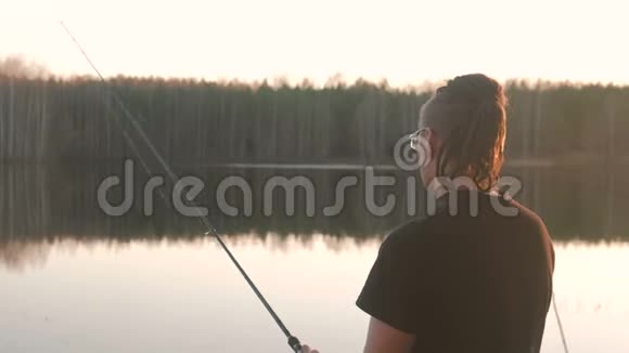池塘上的渔夫戴眼镜的年轻人穿着t恤用鱼竿钓鱼视频的预览图