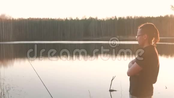 池塘上的渔夫一个戴眼镜戴着t恤钓鱼鱼竿的年轻人视频的预览图