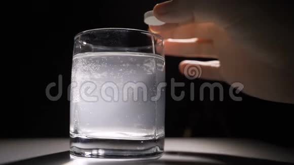 将维他命矿物补充剂泡腾片倒入杯水中拍摄于黑暗背景的工作室视频的预览图