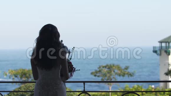 新娘穿着白色连衣裙带着花束看着大海视频的预览图