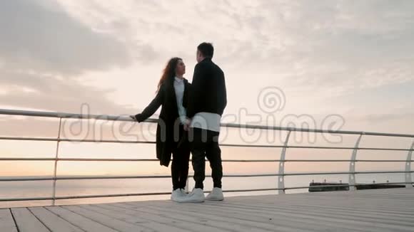 年轻幸福的情侣相爱站在靠近大海或海洋的木墩上彼此微笑黑人视频的预览图