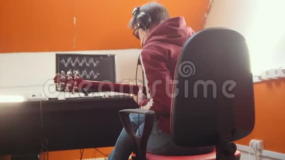 一个戴着耳机的音乐家坐在录音室的电脑旁录制一首歌视频的预览图