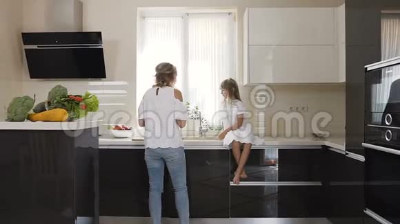 年轻的女人和穿着白色衣服的女孩在厨房里吃美味的红苹果妈妈和她女儿视频的预览图