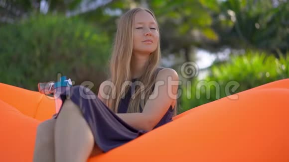 在热带海滩上一位年轻女子坐在充气沙发上喝着多种饮料中的水视频的预览图