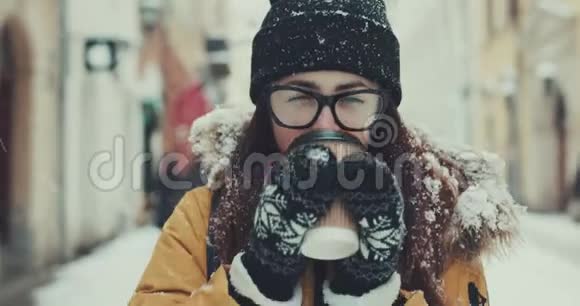 美丽的女孩带着一杯咖啡在冬天的城市里走来走去看着相机微笑着视频的预览图