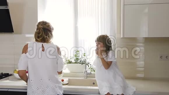漂亮的妈妈和女儿穿着白色衣服在厨房里用西红柿做沙拉健康和纯素食品概念视频的预览图