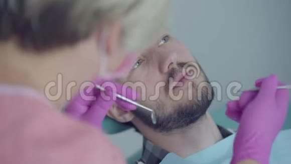 牙医在医疗面罩和手套检查病人的嘴使用医疗工具女性专业医生视频的预览图
