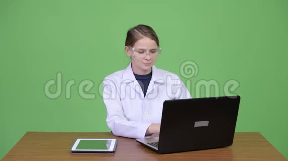 年轻漂亮的女医生戴着护目镜在工作和问候某人视频的预览图