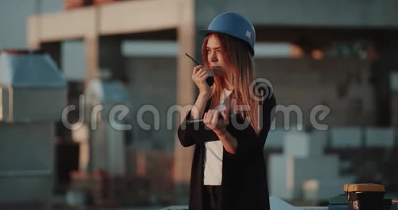 在那个戴着安全帽的年轻女子的屋顶上用收音机说话看着平板电脑视频的预览图