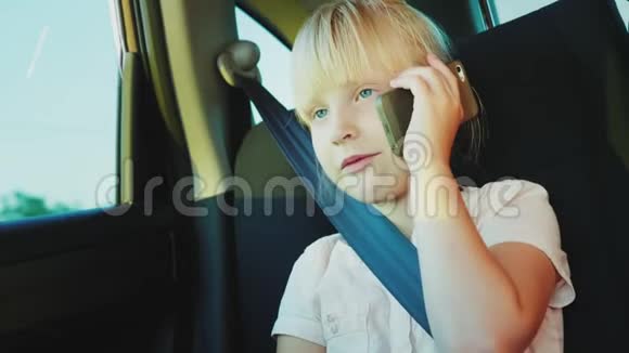 有趣的女孩6岁打电话坐在车后座用安全带系好视频的预览图