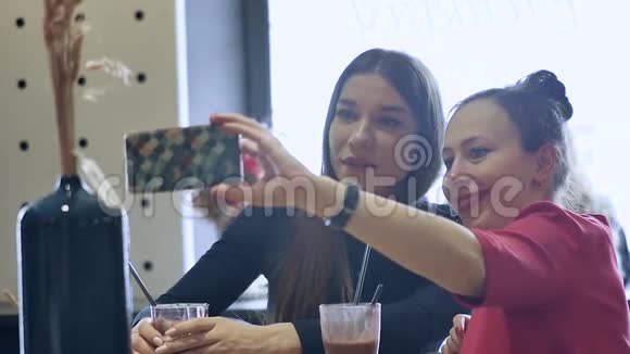 两个漂亮的年轻女人在午餐时放松坐在咖啡馆里在你的智能手机上做自拍商务午餐视频的预览图