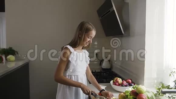 漂亮的穿着白色连衣裙的少女正在厨房准备水果沙拉健康有意识的女孩正在切割视频的预览图
