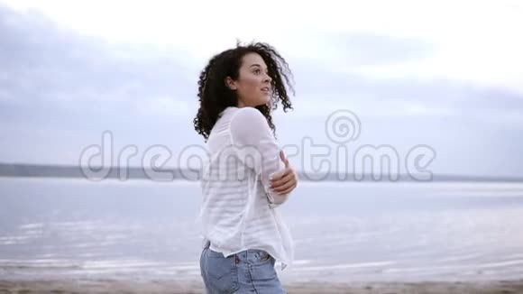 特写镜头一位迷人的年轻女子穿着白衬衫在海边散步卷曲的黑发视频的预览图