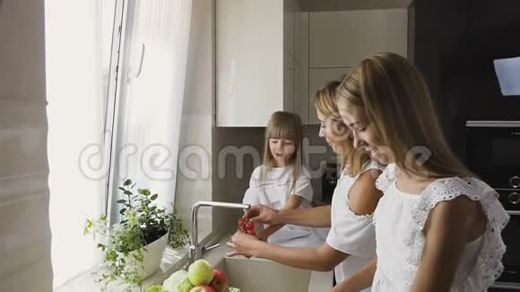 漂亮的快乐妈妈和她的小女儿一起在厨房的水槽里洗蔬菜做饭混合视频的预览图