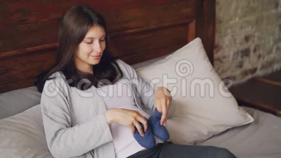 正在玩耍的准妈妈正在怀孕的肚子上踩着蓝色的小鞋子微笑着躺在家里的阁楼上视频的预览图