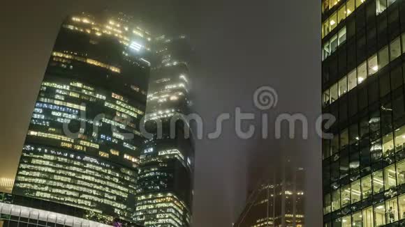 在一个多雾的夜晚摩天大楼和商务中心的办公室窗户时间流逝视频的预览图