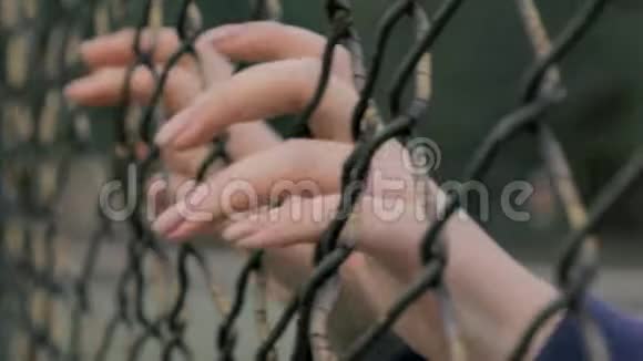 近景的年轻女子手摇动金属网在围栏地区无助的女人摇着金属栅栏视频的预览图