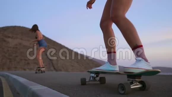 两个女孩滑板车骑在一个木板上的斜坡与天空从山上慢动作稳定视频的预览图