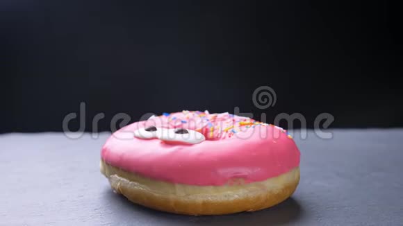 特写镜头围绕着一个美味的釉粉色甜甜圈上面有五颜六色的薯片眼睛在灰色上慢慢旋转视频的预览图
