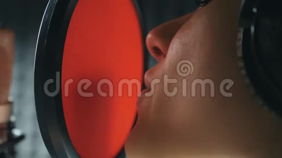 女歌手在音响室演唱歌曲的嘴年轻女孩录制新歌戴着耳机的女人唱歌视频的预览图