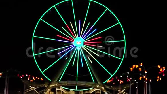摩天轮在夜晚运行灯光照亮大旋转木马上五颜六色的运行灯视频的预览图