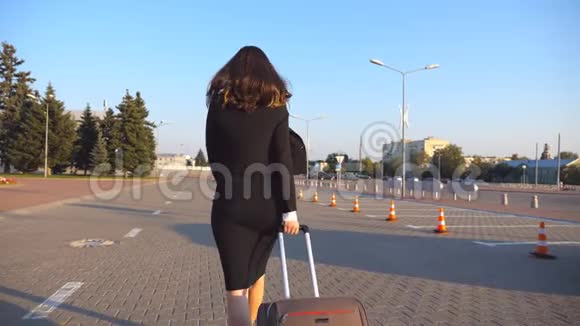 商务女性带着她的手提箱从机场到出租车停车场女士带着行李沿着城市大街走视频的预览图