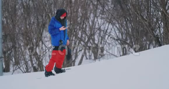 男性滑雪者乘坐滑雪板到雪坡并给你的朋友写信息给智能手机视频的预览图